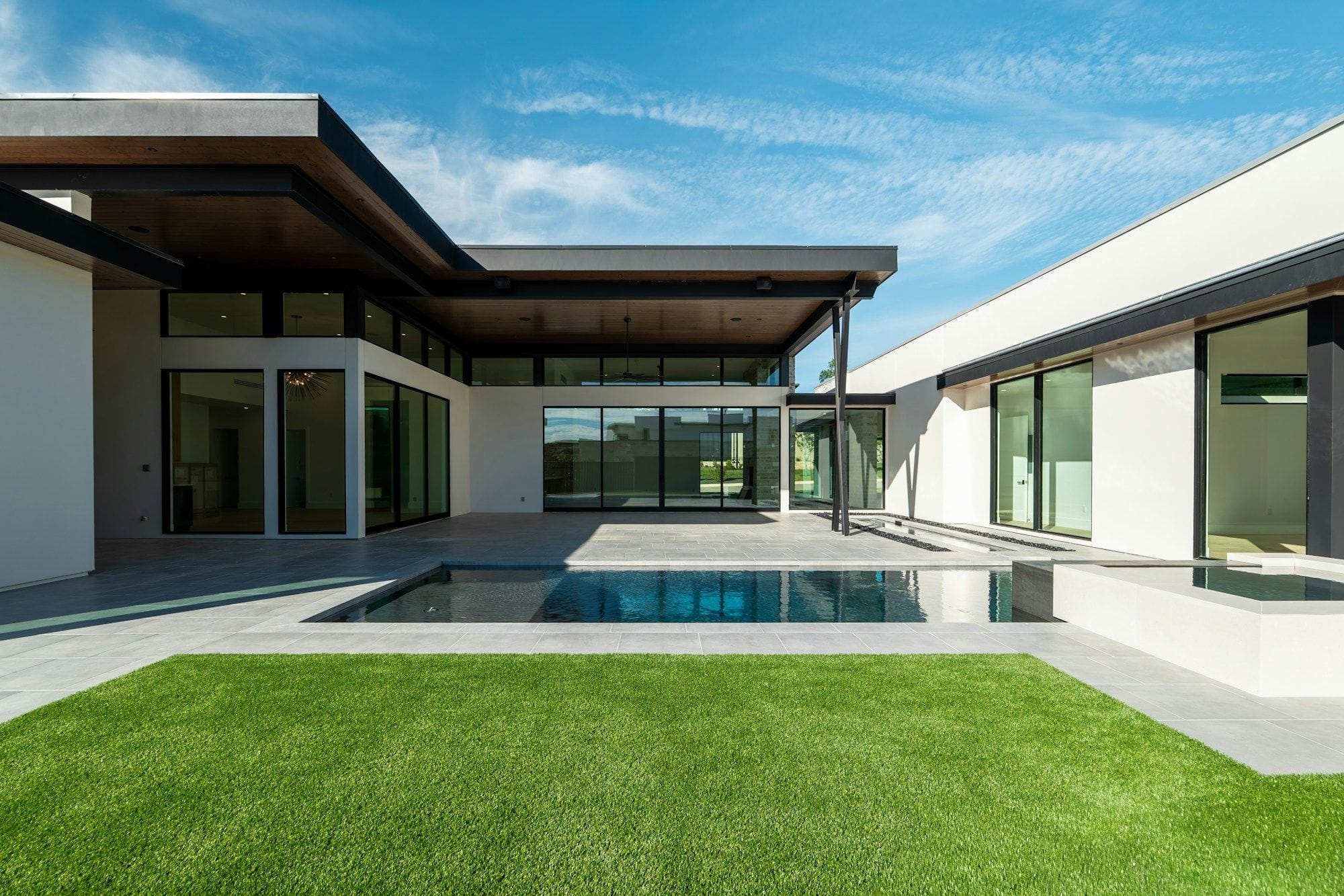 A modern courtyard with a covered patio, reflecting pool and lawn under a clear sky.