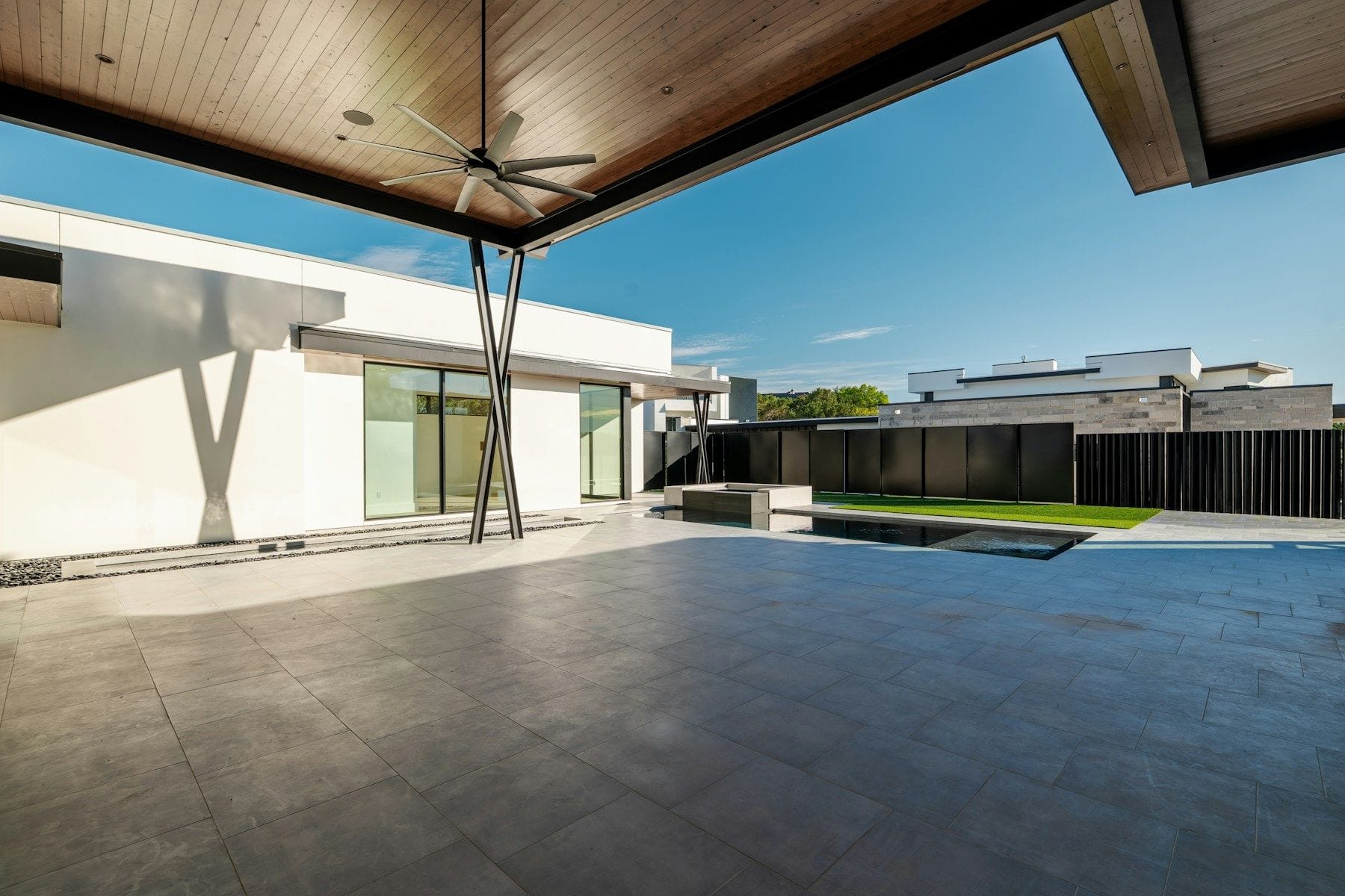 A modern covered patio with a timber-lined ceiling, ceiling fan and large-format stone tiles running out to a pool and lawn.